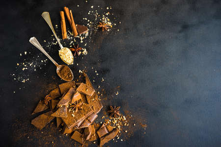 Dark chocolate pieces crushed on dark wooden table, spices like a cinnamon and anise star as a...