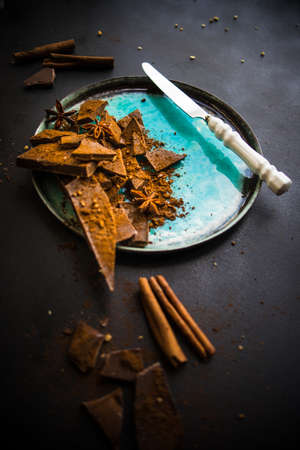 Dark chocolate pieces crushed on dark wooden table, spices like a cinnamon and anise star as a...