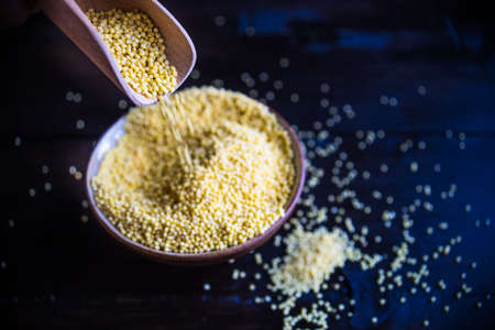 organic raw millet seeds in a rustic bowl on wooden table with copyspace