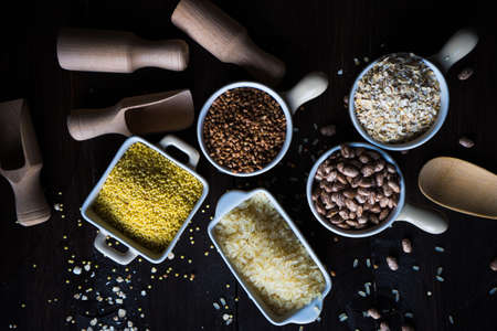 Gluten free cereals millet, brown buckwheat, rice, beans and pasta with copyspace on dark wooden backgroundの写真素材