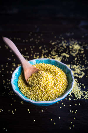 organic raw millet seeds in a rustic bowl on wooden table with copyspaceの写真素材