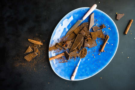 Dark chocolate pieces crushed on dark wooden table, spices like a cinnamon and anise star as a culinary concept with copy space, top viewの写真素材