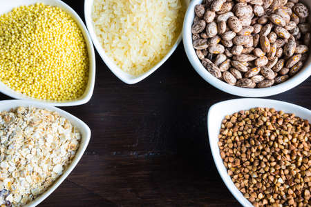 Gluten free cereals millet, brown buckwheat, rice, beans and pasta with copyspace on dark wooden backgroundの写真素材