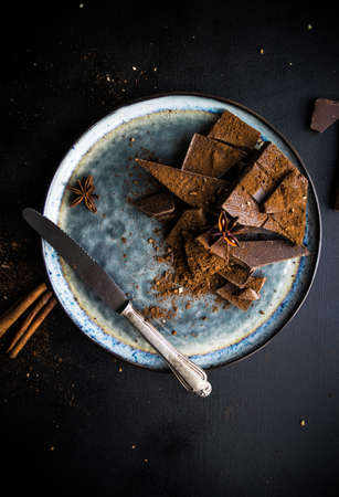 Dark chocolate pieces crushed on dark wooden table, spices like a cinnamon and anise star as a culinary concept with copy space, top viewの写真素材