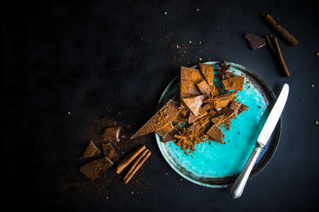 Dark chocolate pieces crushed on dark wooden table, spices like a cinnamon and anise star as a culinary concept with copy space, top viewの写真素材