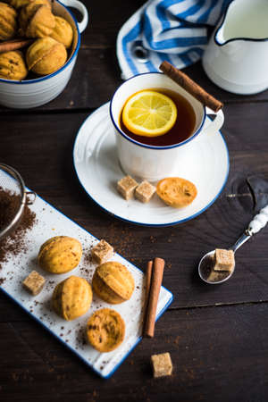 Nut shaped holiday cookies with armored cow and cupof tea with lemon on dark wooden table with copyspaceの写真素材