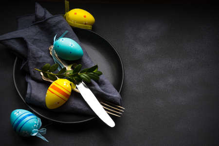 Easter festive table setting with plate, napkin and silverware decorated with colored eggs on rustic...