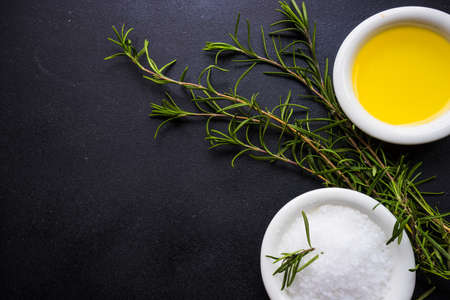 Rosemary herb, sea salt and olive oil in ceramic bowls on rustic wooden background with copyspaceの写真素材