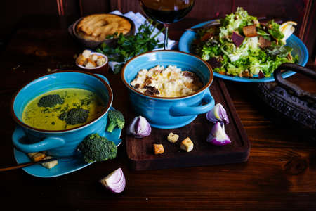 Rustic dinner set with healthy broccoli cream soup, salad and corn milk porridge on dark wooden tableの写真素材