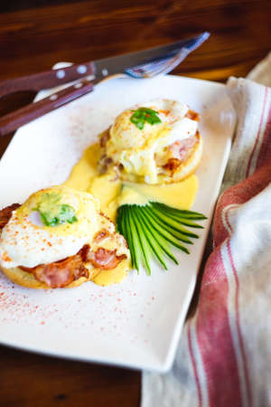 Rustic lunch set with benedict eggs and cucumber salad on dark wooden tableの写真素材