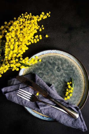 Festive table setting for Easter dinner with bright mimosa flowers on rustic plate