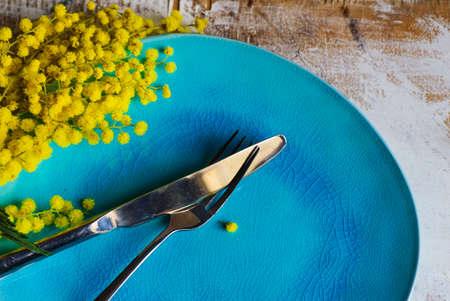 Festive table setting for Easter dinner with bright mimosa flowers on rustic plateの写真素材