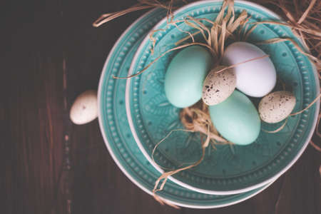 Easter holiday card with colored easter eggs and rustic tableware on dark wooden table with copy spaceの写真素材