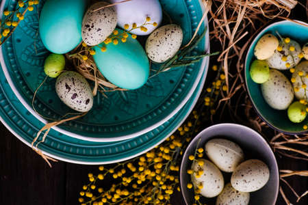 Easter holiday card with colored easter eggs and rustic tableware on dark wooden table with copy spaceの写真素材