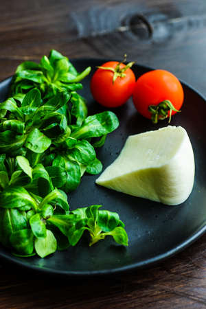 Healthy food concept - fresh corn salad leaves, cheese annd tomatoes on rustic background wih...