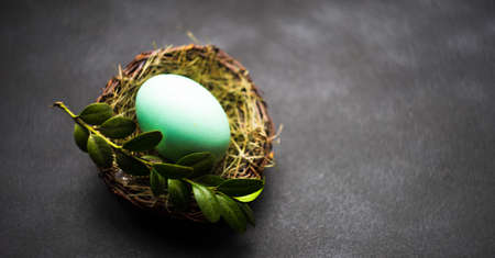 Easter holiday concept with nest full of colored eggs o dark wooden table with copyspaceの写真素材