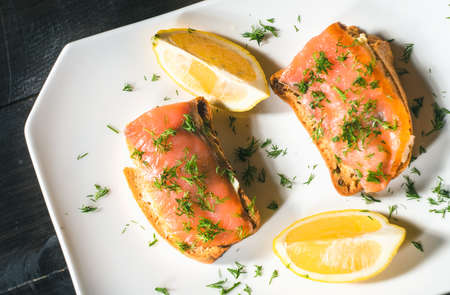 Toast with salmon, herbs and lemon on white plate
