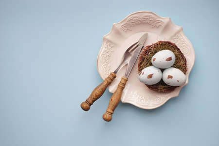 Easter holiday card with table setting with colored eggs on pastel blue backgroundの写真素材