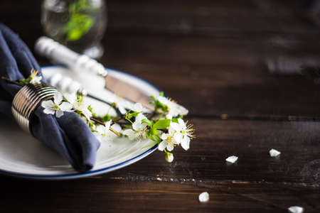 Spring floral concept with blooming cherry tree branches and serving with rustic tablewares on dark...