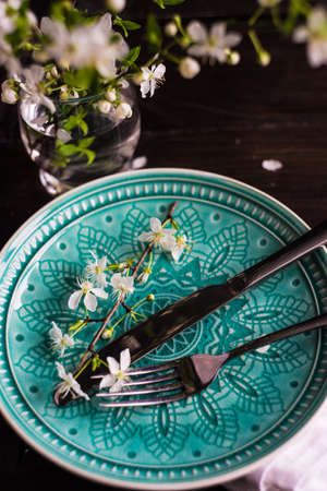 Spring floral concept with blooming cherry tree branches and serving with rustic tablewares on dark wooden tableの写真素材
