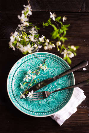 Spring floral concept with blooming cherry tree branches and serving with rustic tablewares on dark wooden tableの写真素材