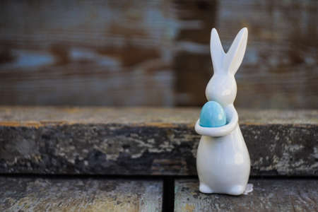 Easter holiday card with easter bunny and blue egg on rustic wooden background with copy space