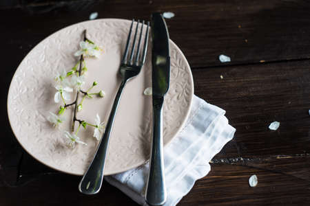 Spring floral concept with blooming cherry tree branches and serving with rustic tablewares on dark...