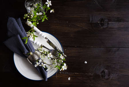 Spring floral concept with blooming cherry tree branches and serving with rustic tablewares on dark wooden tableの写真素材