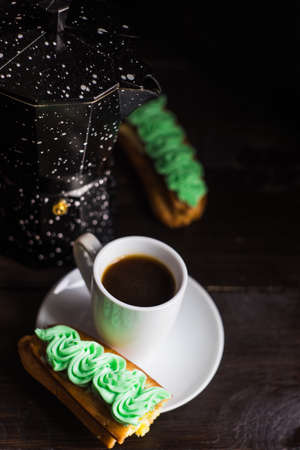 Cup of coffee and eclair on dark wooden table with copyspace
