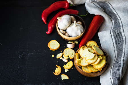 Organic food concept with fresh garlic cloves, red pepper and bread on dark wooden table with copy...