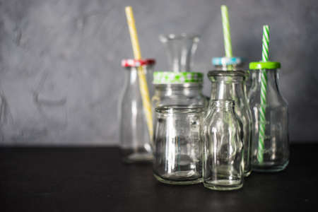 Different shape empty vintage bottles with and without lids and straw standing on black table with...