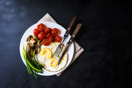 Traditional lunch with fried eggs, cherry tomatoes and green onion on a plate with copy space