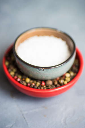 Rustic ceramic bowl with healthy sea salt and different types of pepper corn on concrete background with copy spaceの写真素材