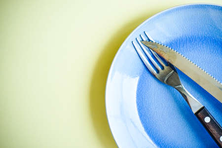 Rustic table setting with blue plate and silverware on yellow backgroundの写真素材