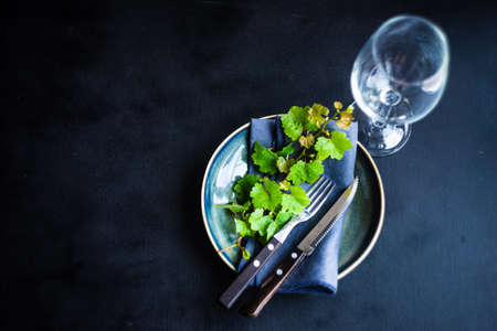 Rustic table setting decorated with green leaves of grape vine on dark wooden table with copy space