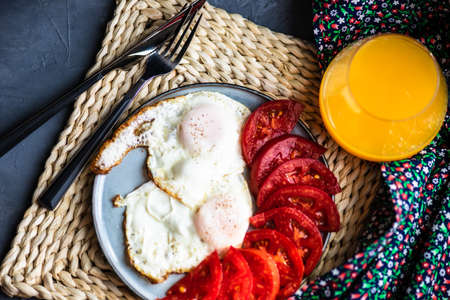 continental breakfast concept with two fried eggs and fresh organic tomato on ceramic plate on concrete background with copy spaceの写真素材