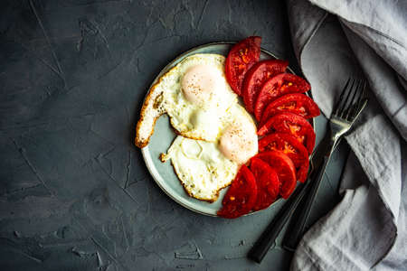 continental breakfast concept with two fried eggs and fresh organic tomato on ceramic plate on concrete background with copy spaceの写真素材