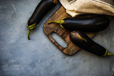 Cooking concept with wooden cutting board and organic eggplants on rustic background with copy spaceの写真素材