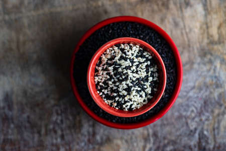 Organic food concept with sesame seeds in red ceramic bowl on a table with copy spaceの写真素材