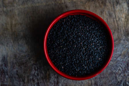 Organic food concept with sesame seeds in red ceramic bowl on a table with copy space