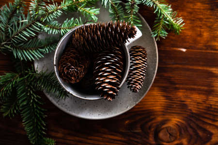 Festive table setting with ceramic plate and cup full of pine cones and decor on wooden backgroundの写真素材