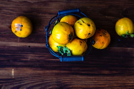 Vintage metal basket full of persimmon fruits on wooden table as a harvest conceptの写真素材