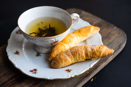 Vintage cup of tea with cinnamon sticks and heartshaped cookies on dark rustic background