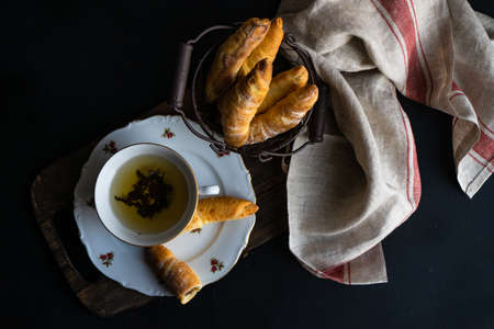 Vintage cup of tea with cinnamon sticks and heartshaped cookies on dark rustic background