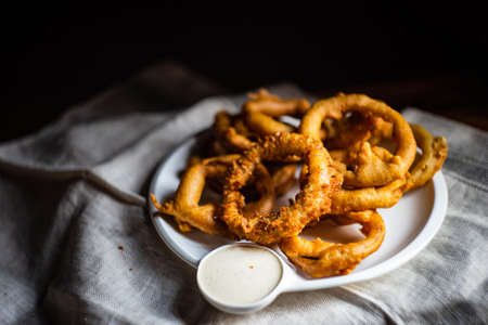 Golden onion rings on rustic table with sauceの写真素材