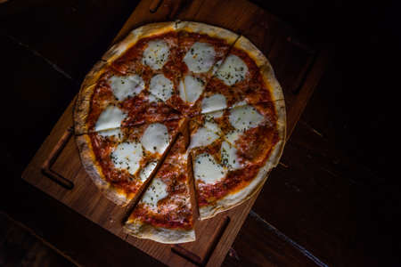 Italian pizza in slices on dark wooden cutting board with copy space
