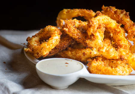 Golden onion rings on rustic table with sauce