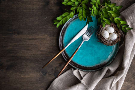 Spring table setting for Easter holiday dinner with boxwood and colored eggs on wooden table with...