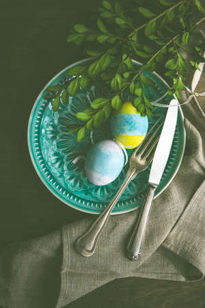 Spring table setting for Easter holiday dinner with boxwood and colored eggs on wooden table with copy spaceの写真素材