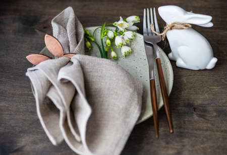 Feastive table setting for holiday Easter dinner decorated with spring snowdrop flowers on rustic...